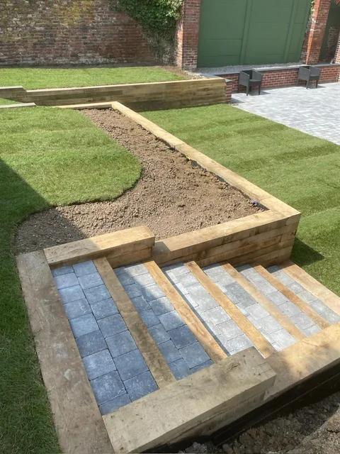 Cheminement pavé, marches et bordures en bois dans un jardin engazonné.