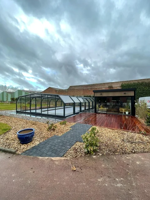 Terrasse en bois, cheminement pavé et massifs plantés autour d’un bâtiment.